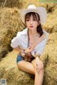 A woman in a cowboy hat sitting on a pile of hay.