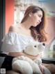 A woman sitting on a window sill holding a teddy bear.