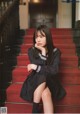 A woman sitting on a red carpeted staircase with her hand on her chin.