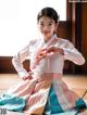 A woman in a pink and blue hanbok sitting on the floor.