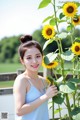 A woman standing next to a tall sunflower in a field.